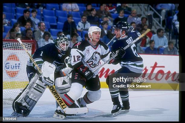 Goaltender Sean Burke and defenseman Adam Burt of the Hartford Whalers sandwich leftwinger Randy Burridge of the Buffalo Sabres during a game at the...