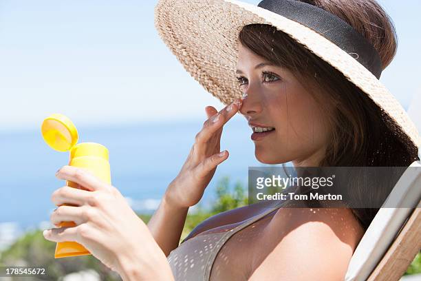 frau mit stroh hut anwenden sonnenschutz für gesicht im freien - suntan lotion stock-fotos und bilder