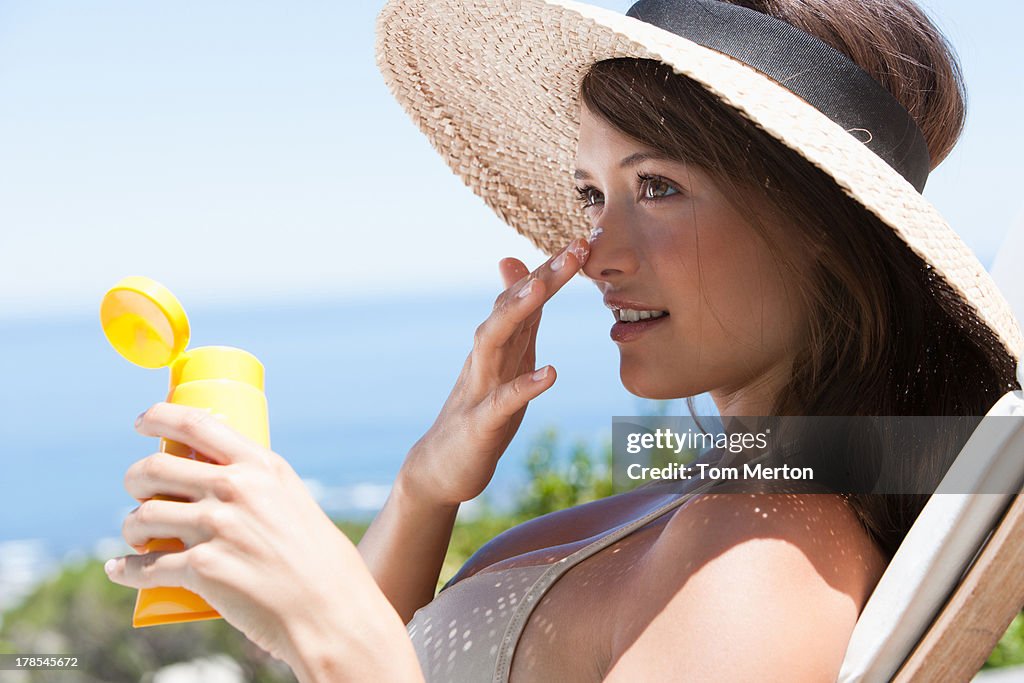 Woman with straw hat applying sunblock to face outdoors