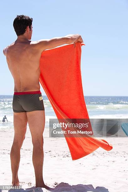 uomo in piedi sulla spiaggia, tenendo l'asciugamano - telo da mare foto e immagini stock