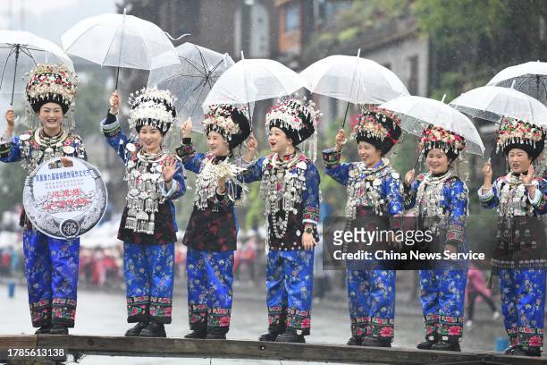 Miao women holding umbrellas stand on a wooden bridge to show traditional Miao costumes during a clothing culture festival at Fenghuang Ancient Town...
