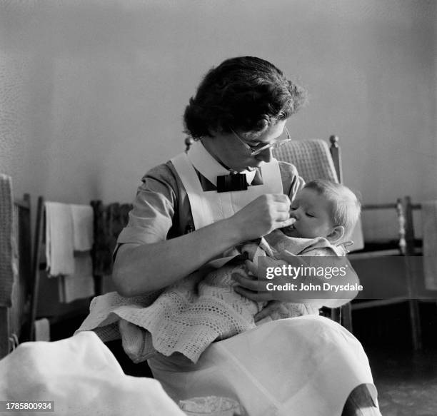 Trainee nanny Jill Flemming feeding a baby in her charge at the Norland Nursery Training College in Chislehurst, Kent, June 1956.