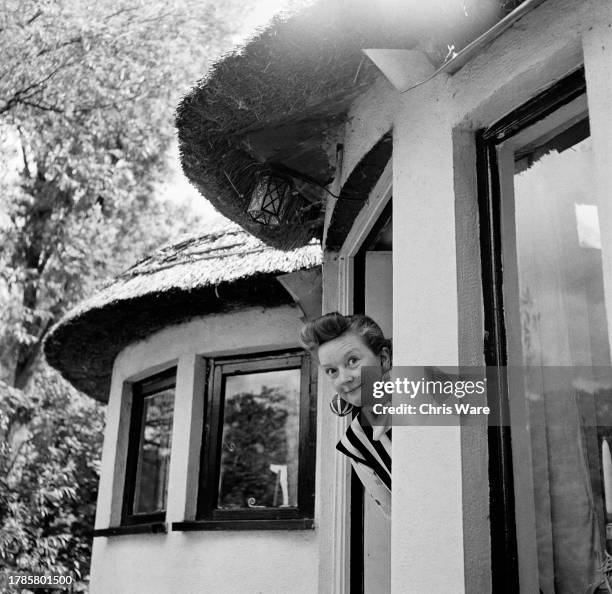 British actress Beryl Reid looking out of the window of Honey Pot Cottage, her Thameside home in Wraysbury, Berkshire, June 1956.