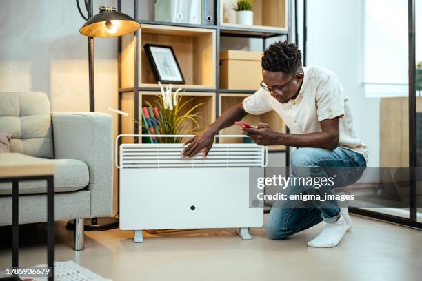 el hombre está ajustando una temperatura usando una tableta con aplicación inteligente para el hogar en la sala de estar moderna - estufa eléctrica fotografías e imágenes de stock