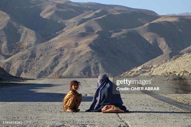 An Afghan burqa-clad woman sits beside a girl, as they look for alms along a street in the Fayzabad district of Badakhshan province on November 16,...