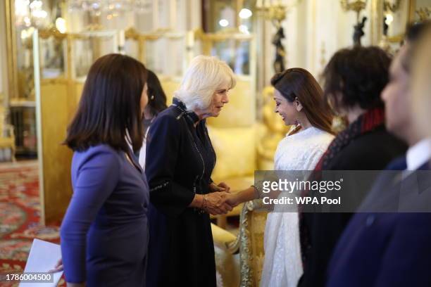 Queen Camilla speaks with guests while Dr Linda Yueh looks on, as she hosts a reception at Buckingham Palace for winners of The Queen's Commonwealth...