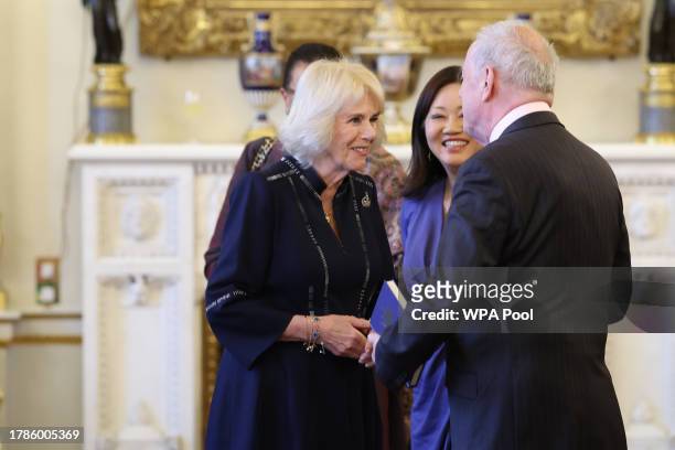 Queen Camilla speaks with Gyles Brandreth as Dr Linda Yueh listens, as she hosts a reception at Buckingham Palace for winners of The Queen's...