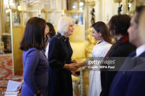 Queen Camilla speaks with guests while Dr Linda Yueh looks on, as she hosts a reception at Buckingham Palace for winners of The Queen's Commonwealth...