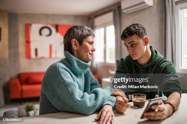 eine mutter und ihr sohn sitzen zu hause und unterhalten sich, während sie ihrem sohn helfen, seine teenager-probleme zu lösen - eltern stock-fotos und bilder