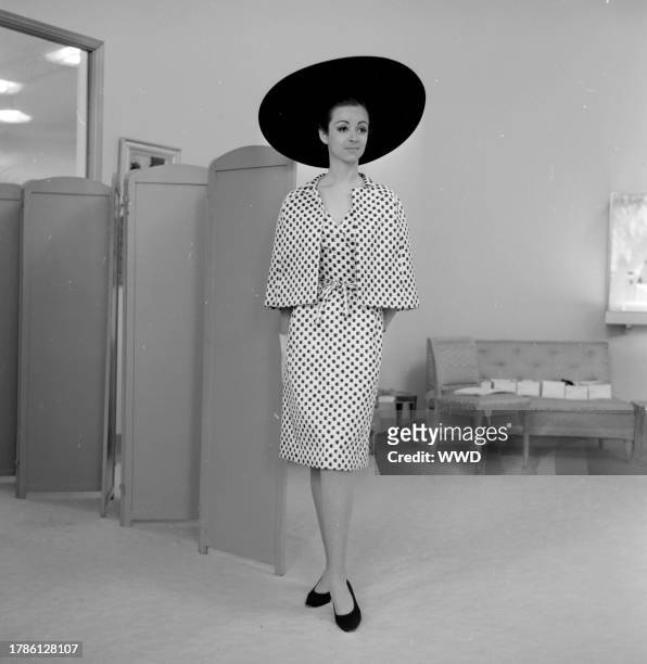 Model poses backstage in a short jacket over sleeveless crisscross dress for the Fall 1965 couture season.