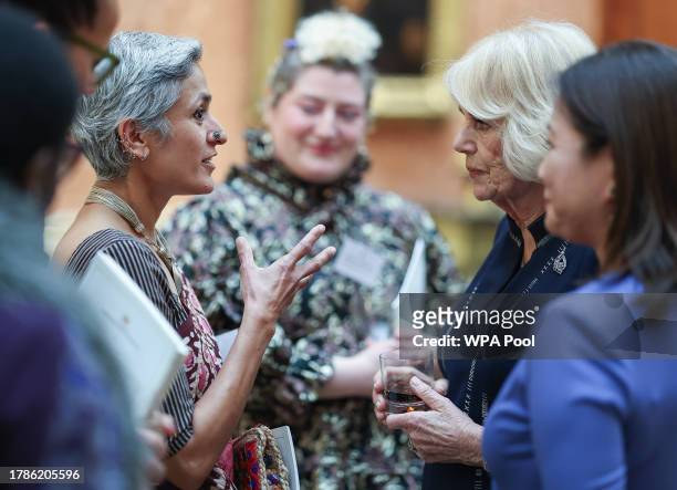 Queen Camilla speaks to a guest as Dr Linda Yueh listens at a reception at Buckingham Palace for winners of The Queen's Commonwealth Essay...