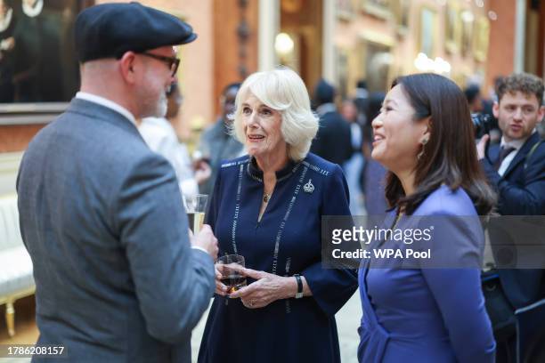 Queen Camilla speaks to Sir Ben Okri as Dr Linda Yueh listens at a reception at Buckingham Palace for winners of The Queen's Commonwealth Essay...
