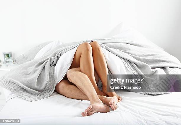 close-up of couple's legs in bed together - caricia fotografías e imágenes de stock