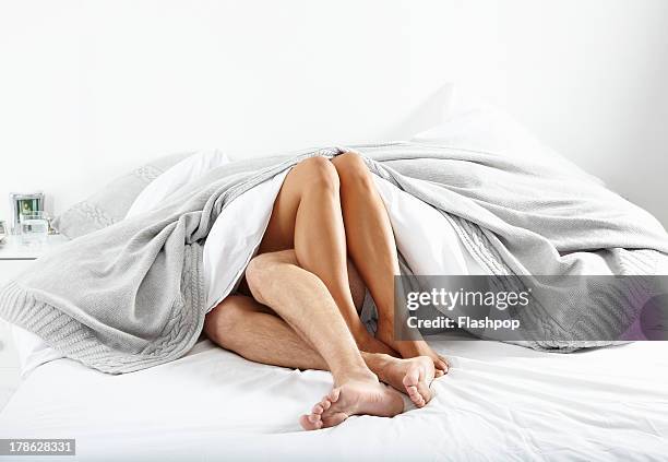 close-up of couple's legs in bed together - beds photos et images de collection