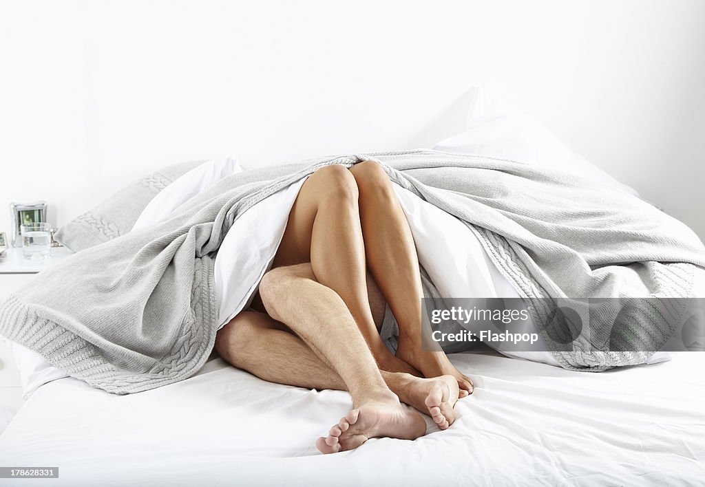 Close-up of couple's legs in bed together