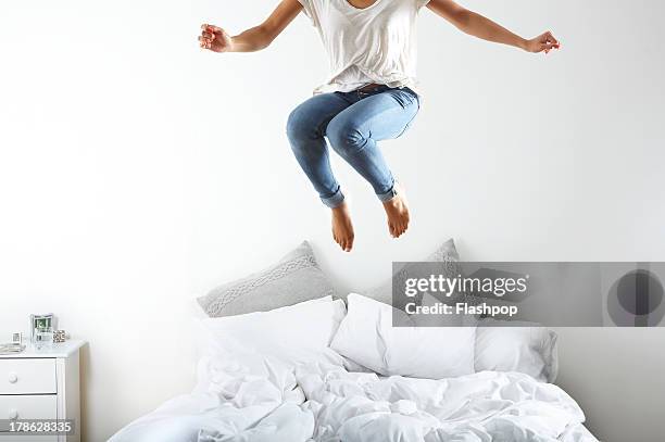 portrait of woman jumping on bed - jeans barefoot fotografías e imágenes de stock