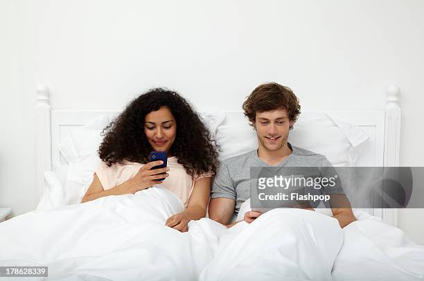 couple using mobile devices in bed - frizzy - fotografias e filmes do acervo