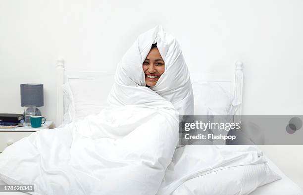 woman wrapped in duvet laughing - piumone foto e immagini stock