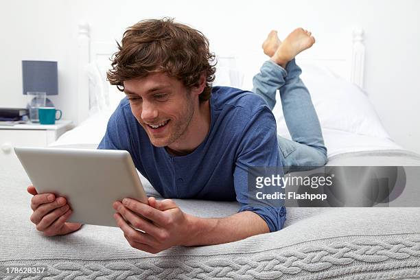 man using digital tablet lying on bed - china foto e immagini stock