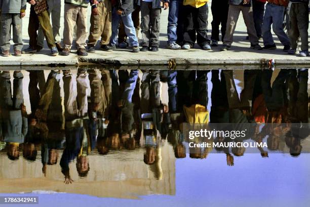 Dozens of Iraqi schoolboys are reflected in a flooded area inside a school while US soldier set up concrete barriers to partially block the area that...