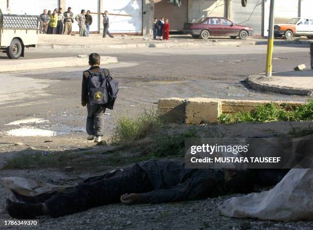 An Iraqi boy walks past two unidentified bodies found dumped in the street in Mosul, 370 kms north of Baghdad, 21 November 2004. Nine men found...