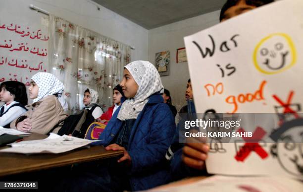 An Iraqi child holds a child's drawing that reads "War is no good" at Hatem al-Taai school in Baghdad 31 December 2002 during a visit by a delegation...