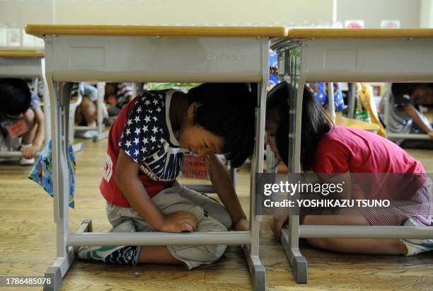 Elementary school children take cover under their desks as part of a nationwide earthquake drill at a Tokyo elementary school on September 1, 2010....