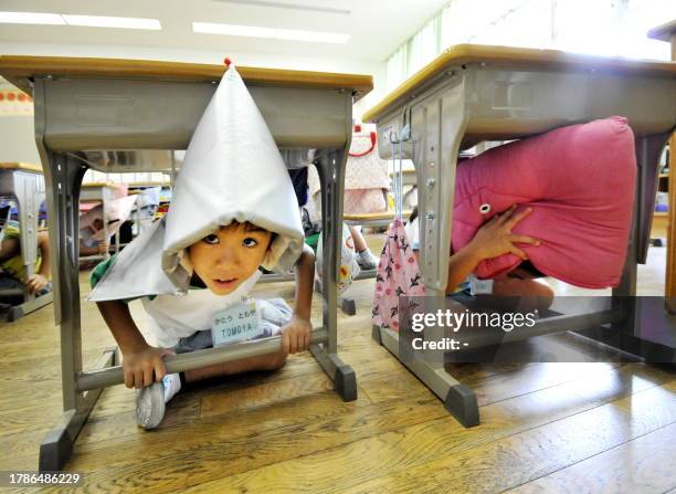 Elementary school children, wearing fire-proof hoods, crouch under their desks as part of a nationwide earthquake drill at a Tokyo elementary school...
