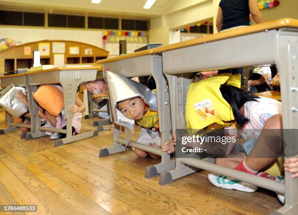 Elementary school children, wearing fire-proof hoods, crouch under their desks as part of a nationwide earthquake drill at a Tokyo elementary school...