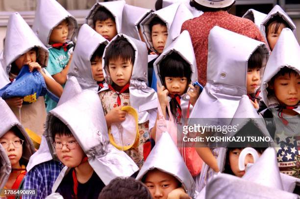 Wearing flame-proof hoods, pupils of a Tokyo elementary school wait in line for their parents as part of a nationwide earthquake drill amid genuine...