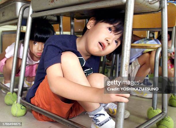 Elementary school children crouch under their desks as part of a nationwide earthquake drill at a Tokyo elementary school, 01 September 2001. The...