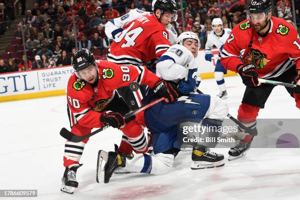 Tyler Johnson and Nick Foligno of the Chicago Blackhawks watch the puck on either side of Nicholas Paul of the Tampa Bay Lightning in the third...