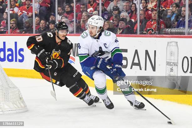 Quinn Hughes of the Vancouver Canucks skates with the puck past Jonathan Huberdeau of the Calgary Flames during the third period of an NHL game at...