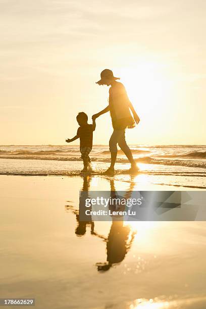 mother and child walking on the beach - backlit family stock pictures, royalty-free photos & images