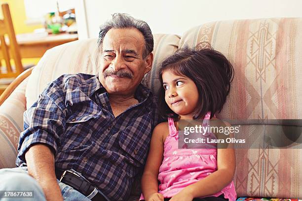 grandfather and granddaughter laughing on couch - latino family stock-fotos und bilder