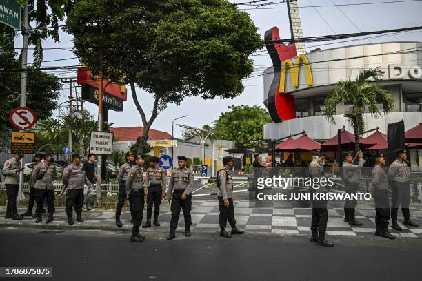 Policemen stand guard in front of a McDonald's branch as people take part in a demonstration in Surabaya on November 17, 2023 in solidarity with the...