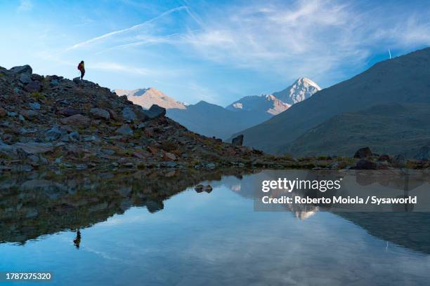 silhouette of hiker admiring mountains reflected in a lake - sondrio fotografías e imágenes de stock