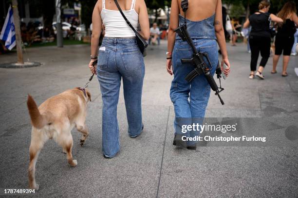 Woman carries an assault rifle as she and a friend walk a dog in downtown Tel Aviv on November 11, 2023 in Tel Aviv, Israel. A month after Hamas's...