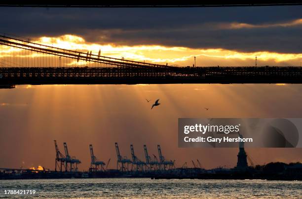 The sun sets behind the Statue of Liberty and the Brooklyn Bridge on November 11 in New York City.