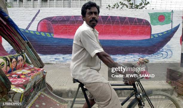 Rickshaw-driver cycles past a wall painted with the election symbol of former Prime Minister Sheikh Hasina Wajed's Awami League in the main business...