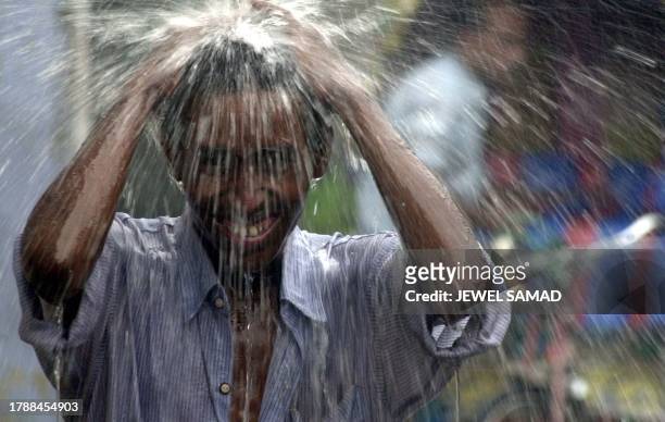 Young rickshaw driver enjoys a bath under rainwater as a home-bound man runs for cover from rain in Dhaka, 31 July 2001. Bangladesh's northeastern...