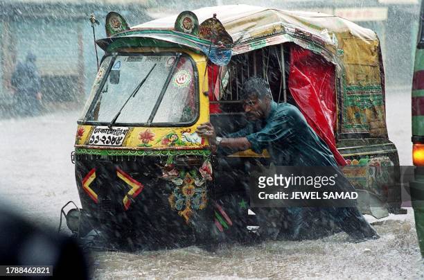 An auto rickshaw driver pushes his vehicle to get it out of the water during heavy rain, 28 October 2000, in Dhaka. Storm lashed the capital and the...