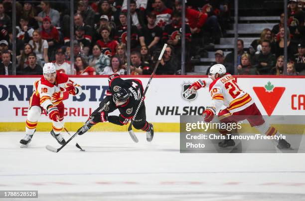 Mathieu Joseph of the Ottawa Senators is hooked by Blake Coleman of the Calgary Flames as his teammate Nikita Zadorov reaches for the puck during the...