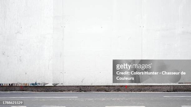 white painted wooden panel wall with gray asphalt street in paris, france - palissades stockfoto's en -beelden