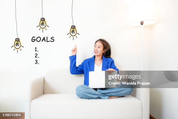 2024 goals with young woman cheerful and happy new year with laptop on the sofa in living room.  star together new year 2024 - happy new month stockfoto's en -beelden