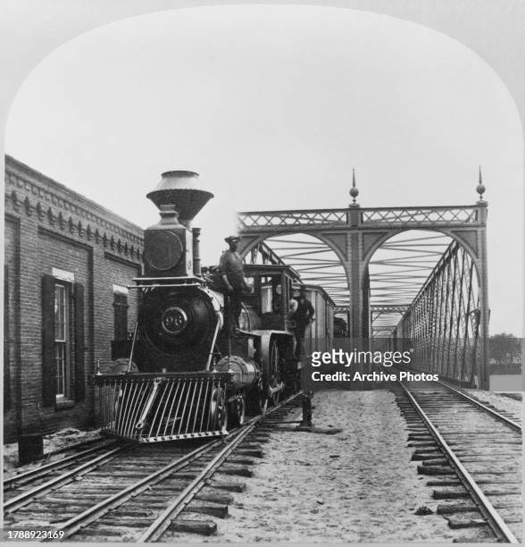 Wisconsin Central Railway steam engine fitted with a cowcatcher, '96' on its number plate, a freight service on an iron railroad bridge spanning the...