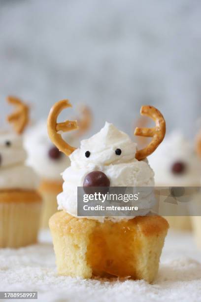 close-up image of homemade, christmas reindeer design cupcakes, buttercream swirl topping decorated with candy coated chocolate sweet noses and salted pretzel antlers, missing bite, apricot jam filling, focus on foreground - cake case stock pictures, royalty-free photos & images