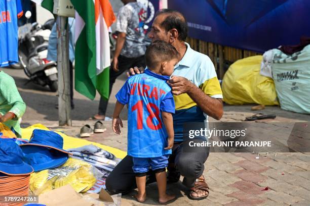 Father tries an India's cricket team jersey on his child at a stall outside the Narendra Modi Stadium in Ahmedabad on November 18 on the eve of the...