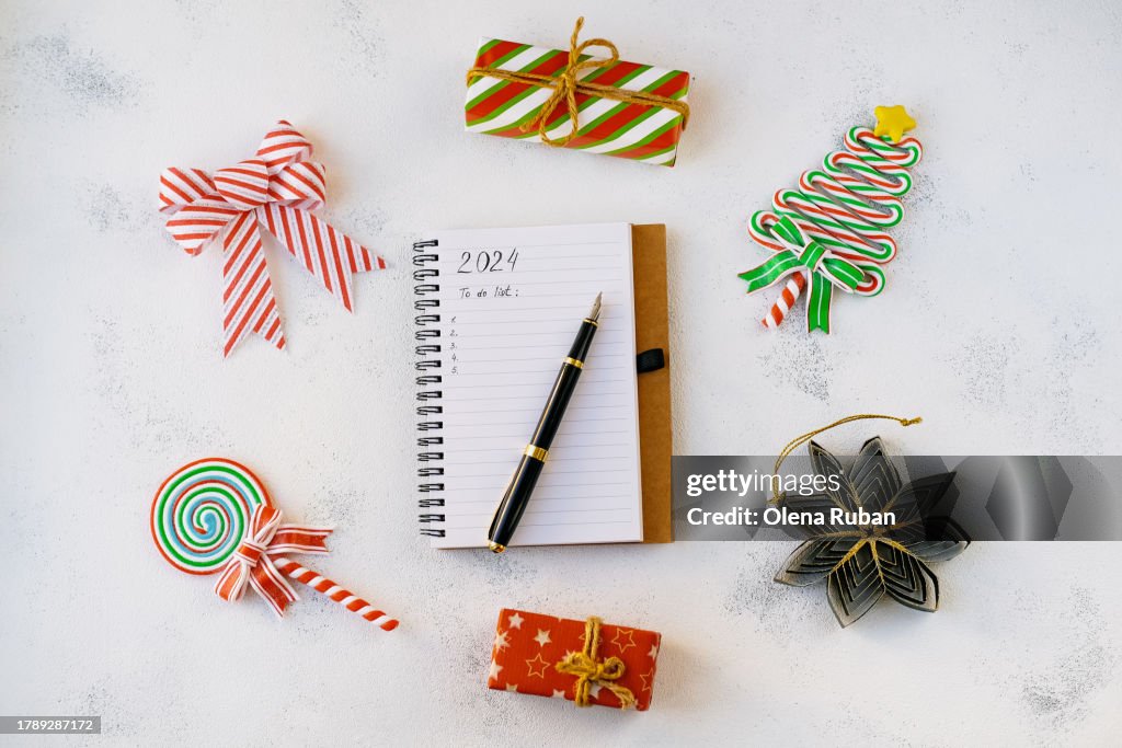 2024 To do list on notepad and pen among gift boxes, lollipops, new year toys.