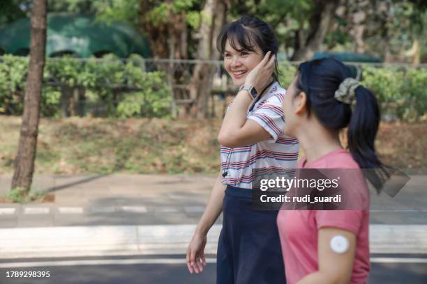 day in the life of young woman with continuous glucose monitor jogging for exercise on a park with her friend - continuous glucose monitor stock pictures, royalty-free photos & images